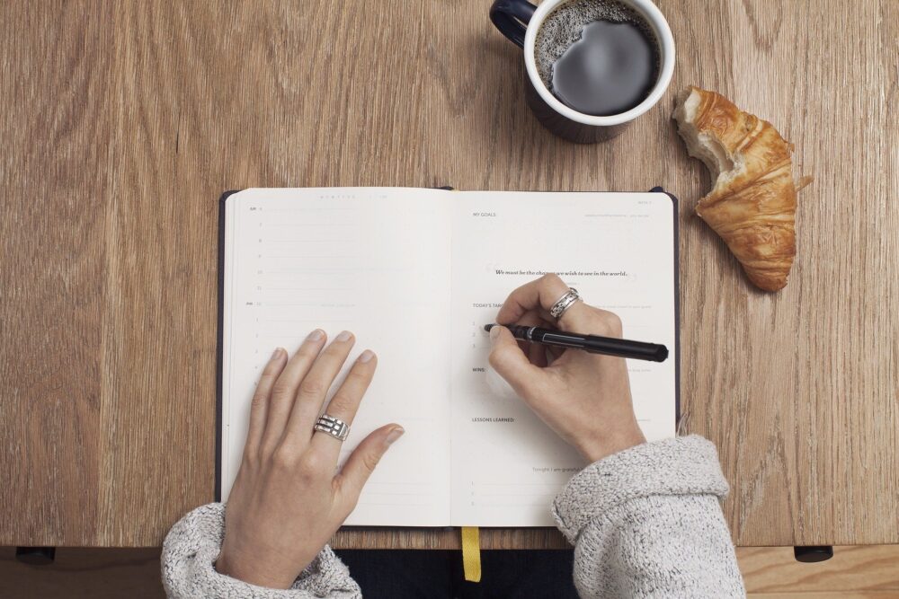 woman writing with a coffee & croissant